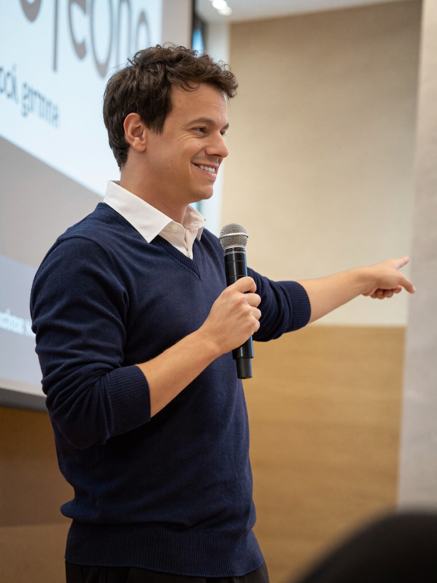 Vinicius Oliveira falando ao microfone em uma palestra e apontando para o lado